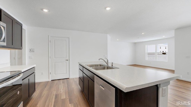 kitchen featuring stainless steel appliances, light countertops, light wood-style floors, a sink, and a textured ceiling