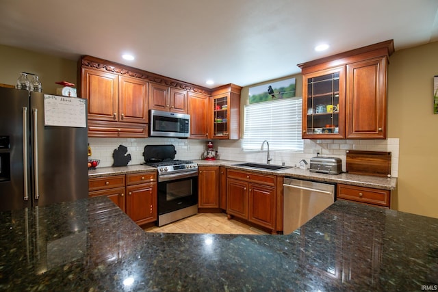 kitchen with backsplash, dark stone counters, stainless steel appliances, and a sink