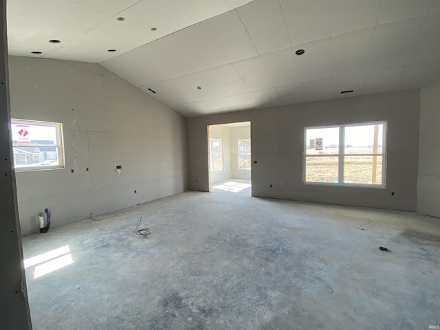 unfurnished room with a healthy amount of sunlight, unfinished concrete floors, and lofted ceiling