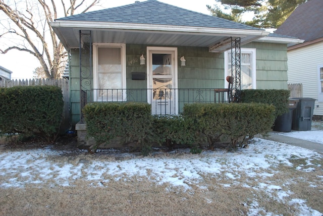 snow covered property entrance featuring a porch and roof with shingles