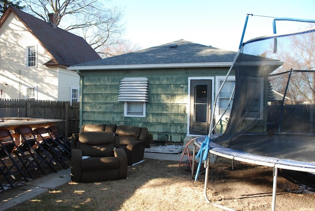 rear view of house featuring a trampoline, fence, and a shingled roof