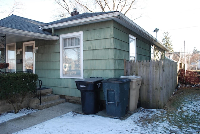 view of snowy exterior with a chimney and fence