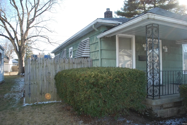 view of side of home featuring a porch, fence, and a chimney