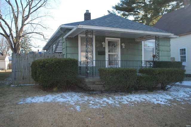 view of front of house with a porch, a shingled roof, and a chimney