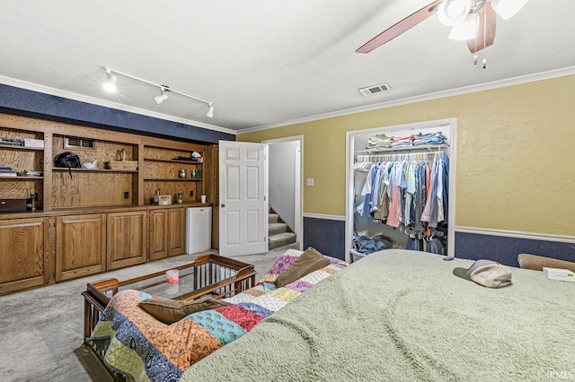 bedroom featuring a textured wall, ornamental molding, visible vents, and light colored carpet