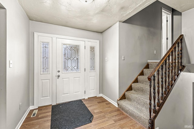 foyer entrance featuring visible vents, light wood-style flooring, and baseboards