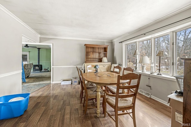 dining space featuring a wood stove, crown molding, baseboards, and wood finished floors