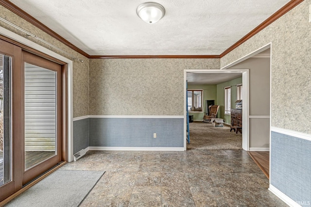 empty room with wallpapered walls, ornamental molding, a textured ceiling, and wainscoting