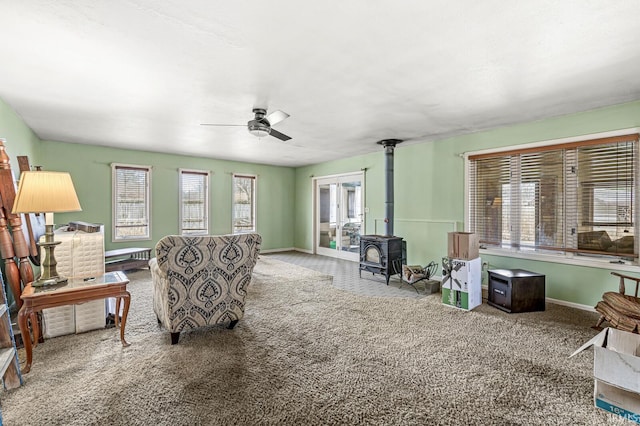 carpeted living area with a wood stove, baseboards, and a ceiling fan