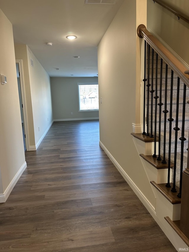 hallway featuring stairs, dark wood-style flooring, visible vents, and baseboards