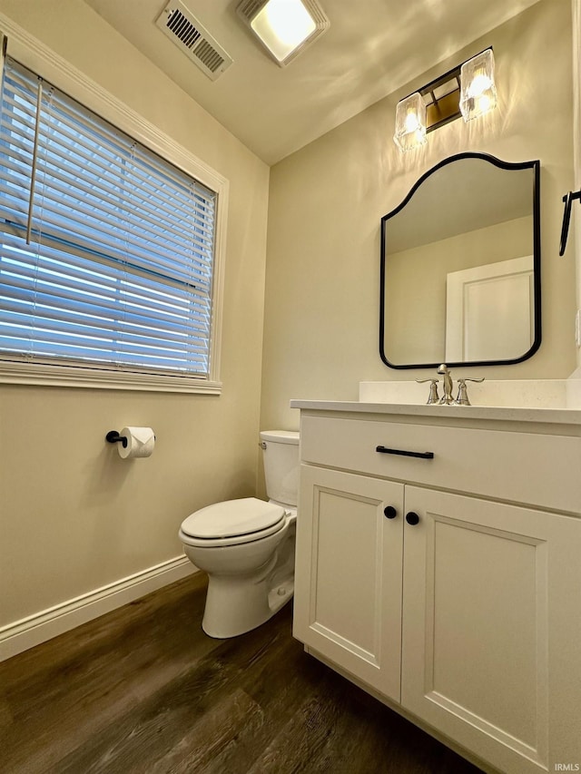 half bathroom with visible vents, toilet, vanity, wood finished floors, and baseboards