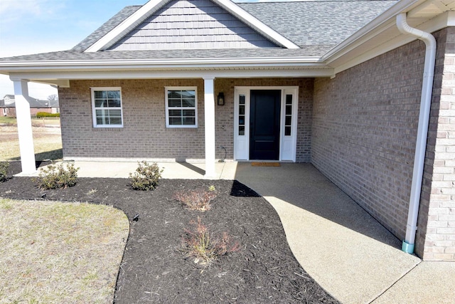 property entrance featuring brick siding and roof with shingles