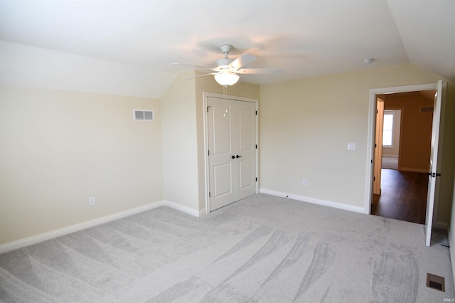 interior space featuring carpet floors, lofted ceiling, visible vents, a ceiling fan, and baseboards