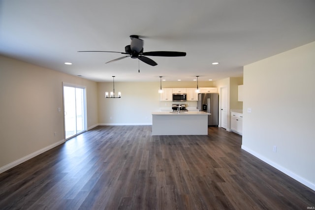 unfurnished living room featuring ceiling fan with notable chandelier, dark wood-type flooring, recessed lighting, and baseboards