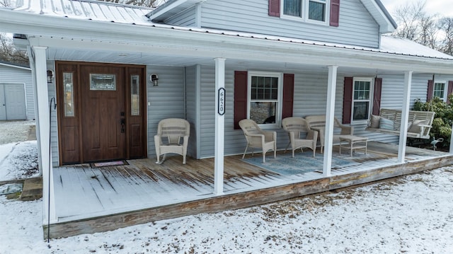 snow covered property entrance with covered porch and metal roof