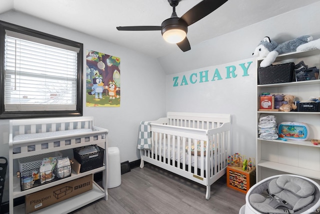 bedroom featuring lofted ceiling, ceiling fan, wood finished floors, baseboards, and a nursery area