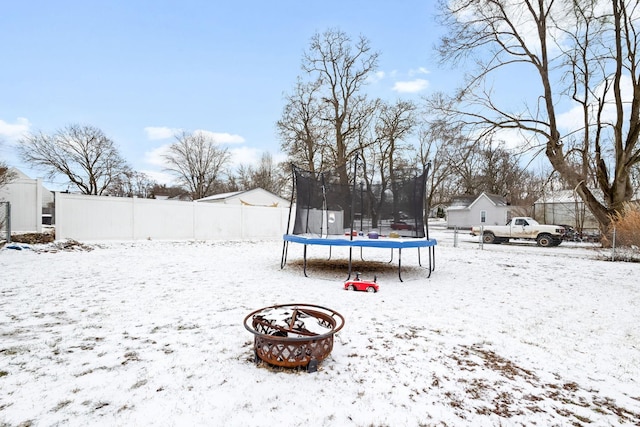 yard layered in snow featuring a trampoline and fence