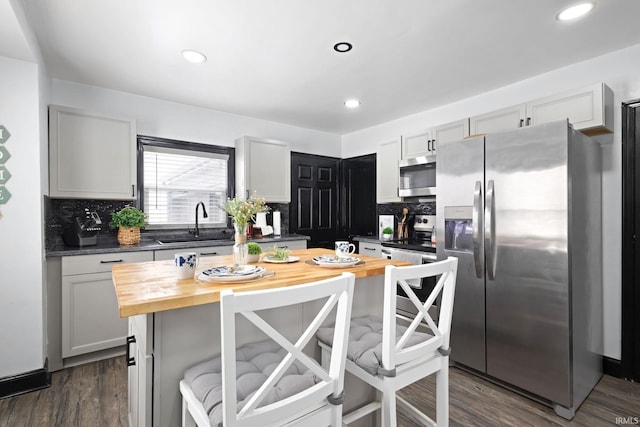 kitchen featuring stainless steel appliances, dark wood-type flooring, a kitchen island, a sink, and wooden counters