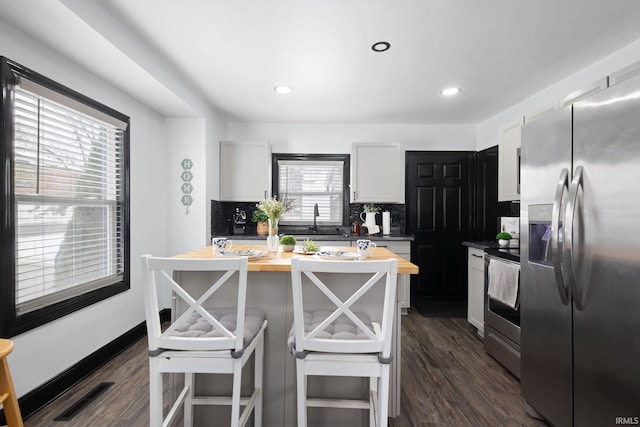 kitchen with visible vents, decorative backsplash, butcher block countertops, dark wood-type flooring, and stainless steel appliances