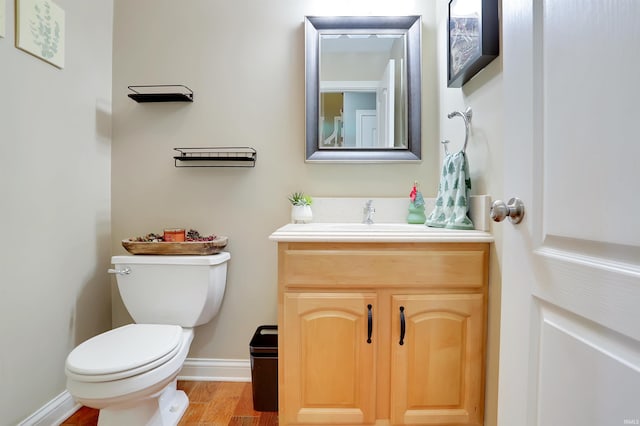 half bathroom with wood finished floors, vanity, toilet, and baseboards