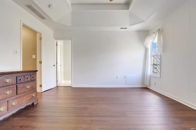 spare room featuring a raised ceiling, visible vents, dark wood finished floors, and baseboards