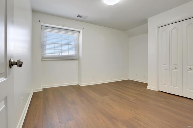 unfurnished bedroom with baseboards, a closet, visible vents, and wood finished floors