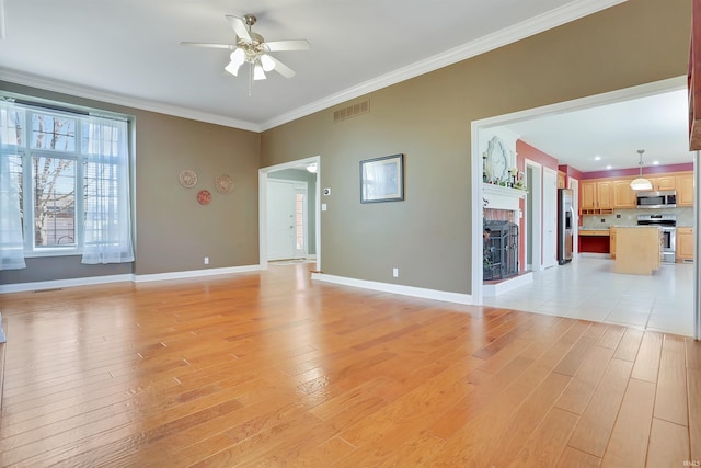 unfurnished living room with light wood-style flooring, a fireplace, a ceiling fan, baseboards, and crown molding