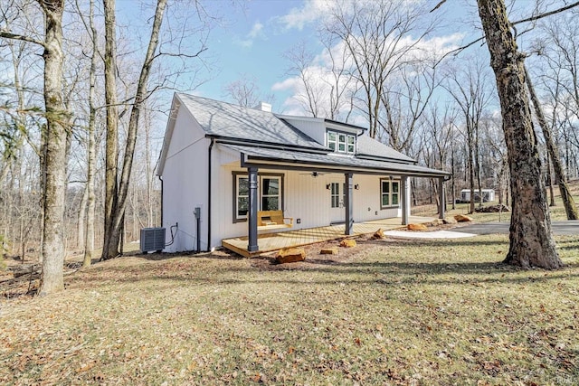 view of front of property featuring central AC unit, covered porch, a shingled roof, a chimney, and a front yard