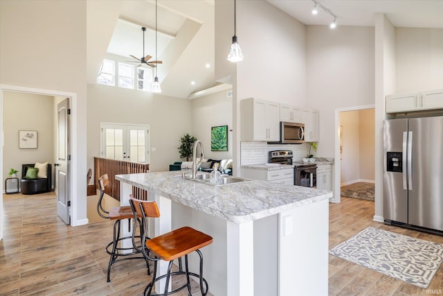 kitchen with a center island with sink, a breakfast bar area, stainless steel appliances, french doors, and a sink