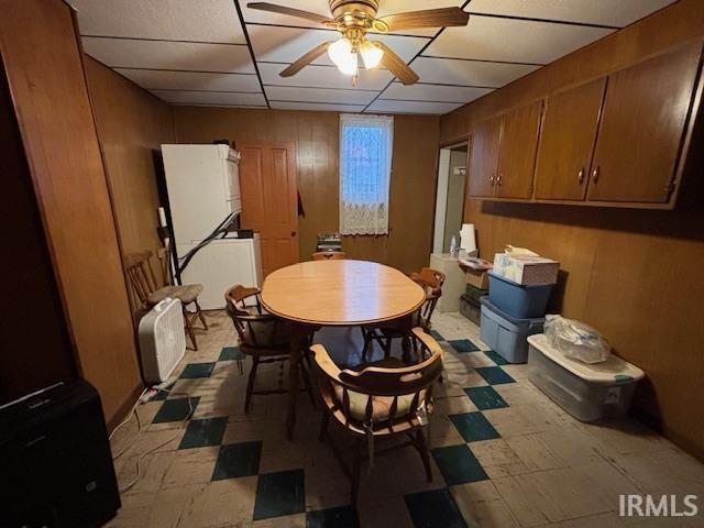 dining space with ceiling fan, light floors, a paneled ceiling, and wooden walls