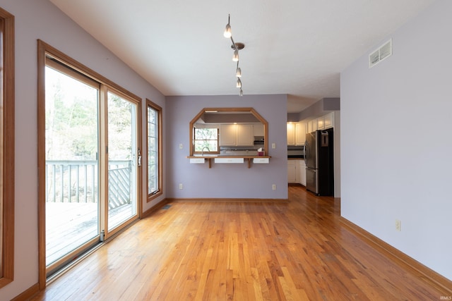 unfurnished living room with a sink, visible vents, baseboards, and light wood-style flooring