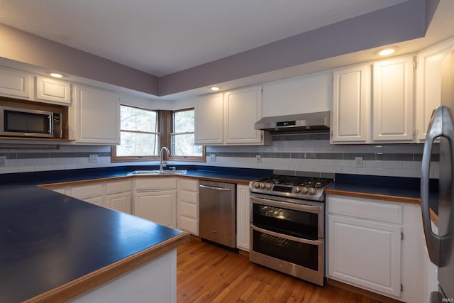 kitchen with a sink, dark countertops, white cabinetry, appliances with stainless steel finishes, and wall chimney range hood