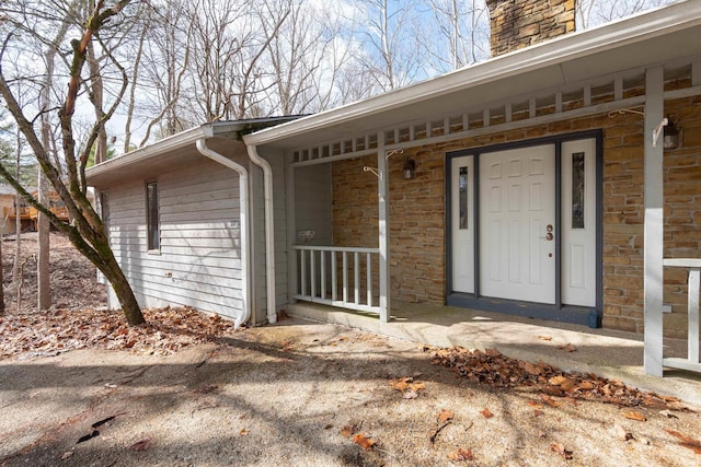 view of exterior entry with stone siding, covered porch, and a chimney