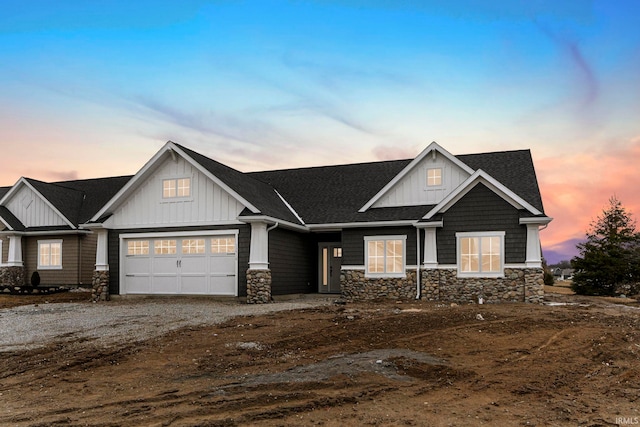 craftsman-style home featuring a garage, a shingled roof, stone siding, gravel driveway, and board and batten siding