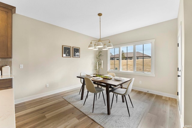 dining space with light wood-type flooring, baseboards, and an inviting chandelier