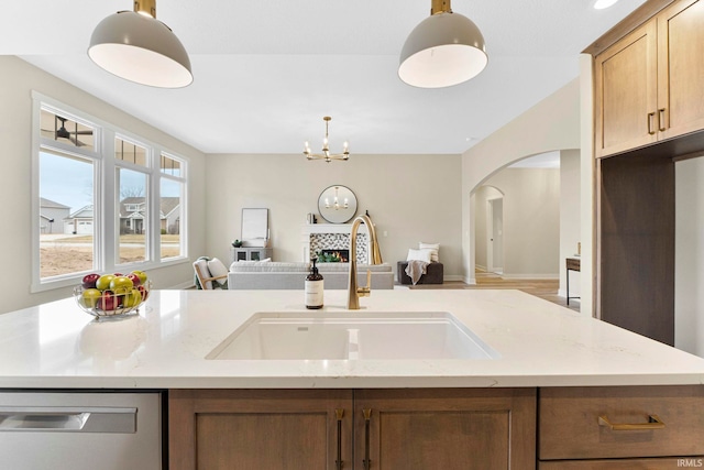 kitchen with light stone counters, stainless steel dishwasher, open floor plan, a sink, and a lit fireplace