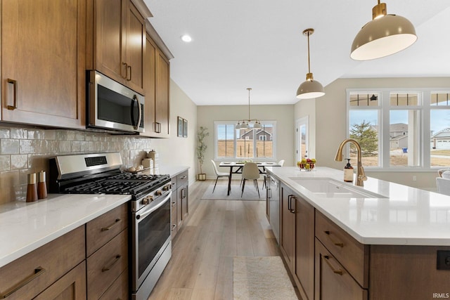 kitchen with a center island with sink, decorative backsplash, light wood-style flooring, appliances with stainless steel finishes, and a sink