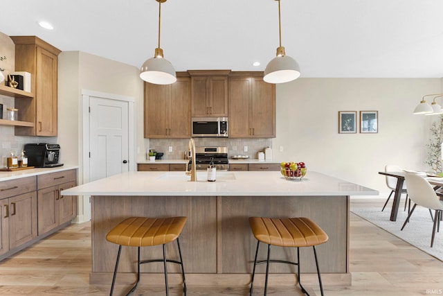 kitchen with a sink, a kitchen breakfast bar, light countertops, appliances with stainless steel finishes, and tasteful backsplash