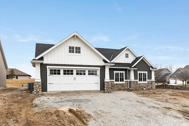 view of front of home featuring board and batten siding, gravel driveway, roof with shingles, and stone siding