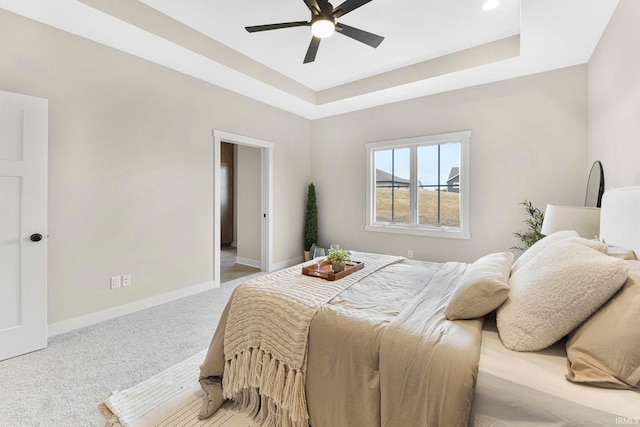 bedroom featuring light carpet, ceiling fan, baseboards, and a tray ceiling