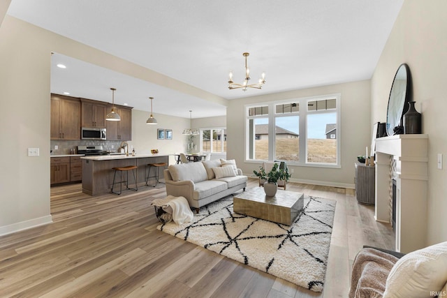 living room with light wood-type flooring, a fireplace, baseboards, and a notable chandelier