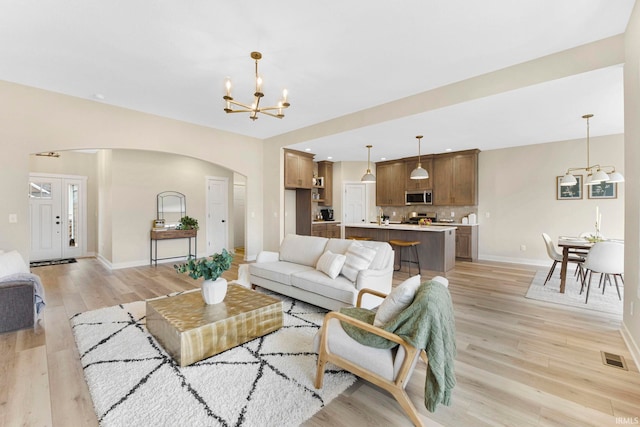 living room featuring light wood-style floors, baseboards, a chandelier, and arched walkways