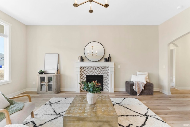 living room featuring arched walkways, wood finished floors, a notable chandelier, and a tile fireplace