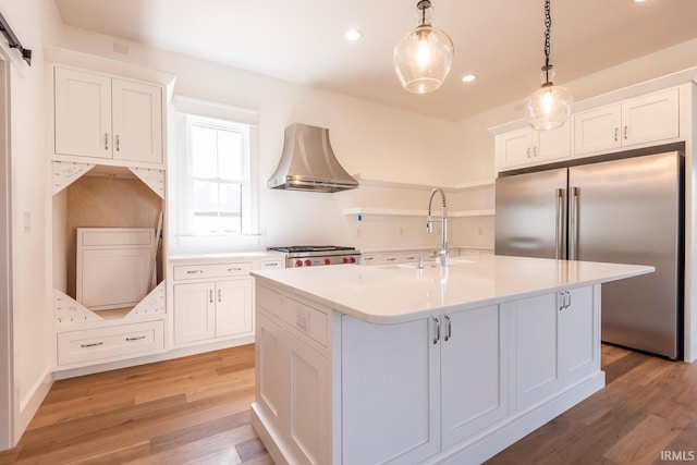 kitchen featuring a sink, a barn door, high end fridge, wall chimney exhaust hood, and range