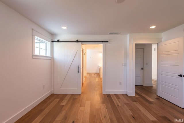 unfurnished bedroom with light wood finished floors, visible vents, baseboards, and a barn door