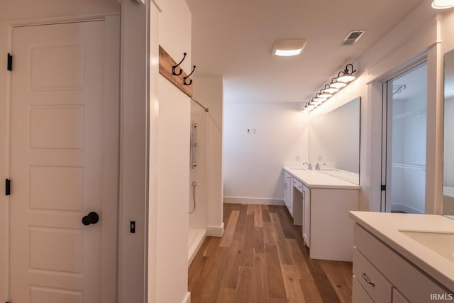 bathroom with visible vents, a shower stall, two vanities, wood finished floors, and a closet