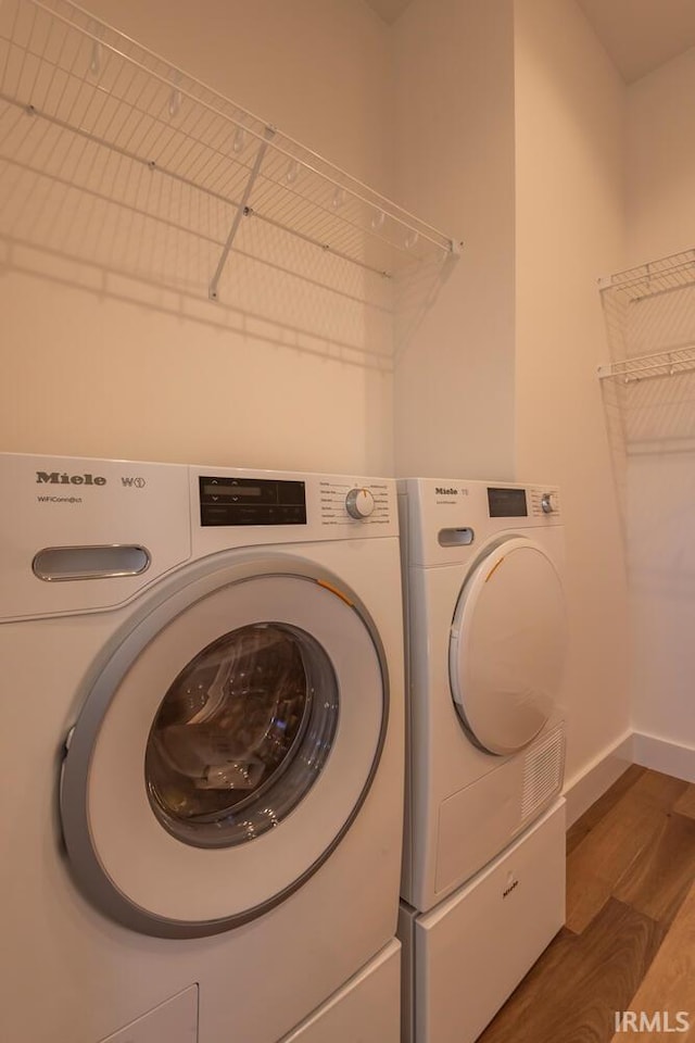 laundry area with laundry area, washer and dryer, baseboards, and wood finished floors