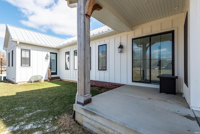 entrance to property with a patio area, a lawn, board and batten siding, and metal roof