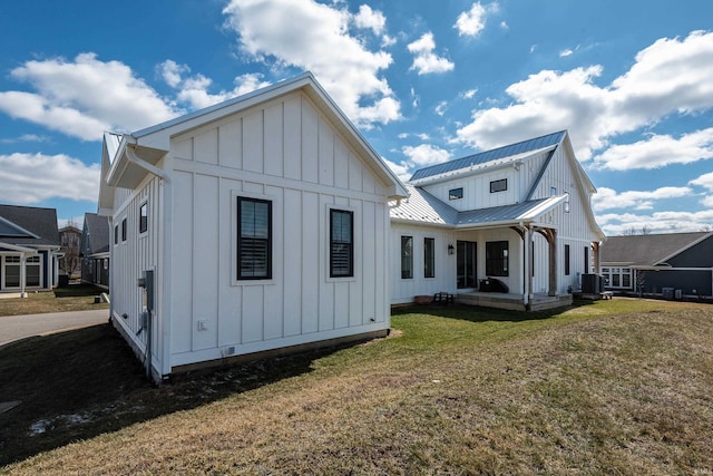 rear view of property featuring board and batten siding, central AC unit, metal roof, a yard, and a standing seam roof