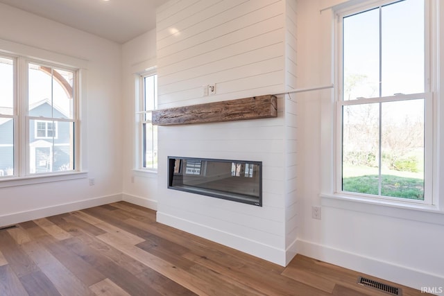 unfurnished living room with visible vents, wood finished floors, baseboards, and a glass covered fireplace